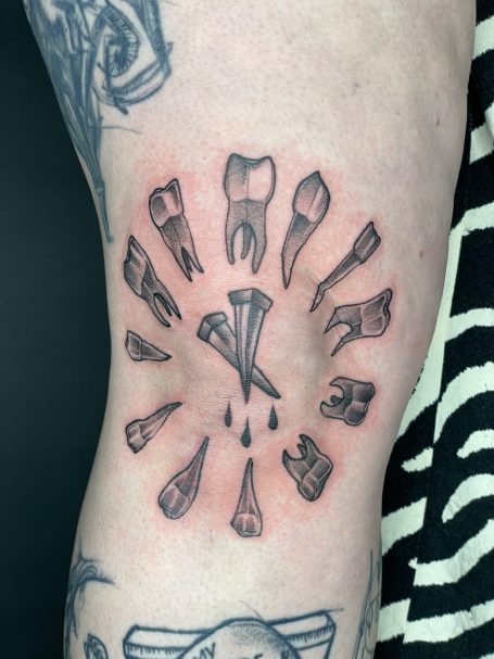 Tattoo mit Zähnen und Instrumenten, die strahlenförmig angeordnet sind.