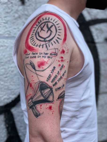 Tattoo auf dem Oberarm mit einem Smiley, Lautsprecher und textlichen Elementen.