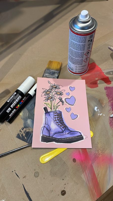Lila Stiefel mit Blumen und Herzen, umgeben von Malutensilien.