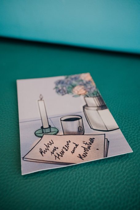 Postkarte mit Notizen, Kerze, Tasse und Vase auf einem Tisch.