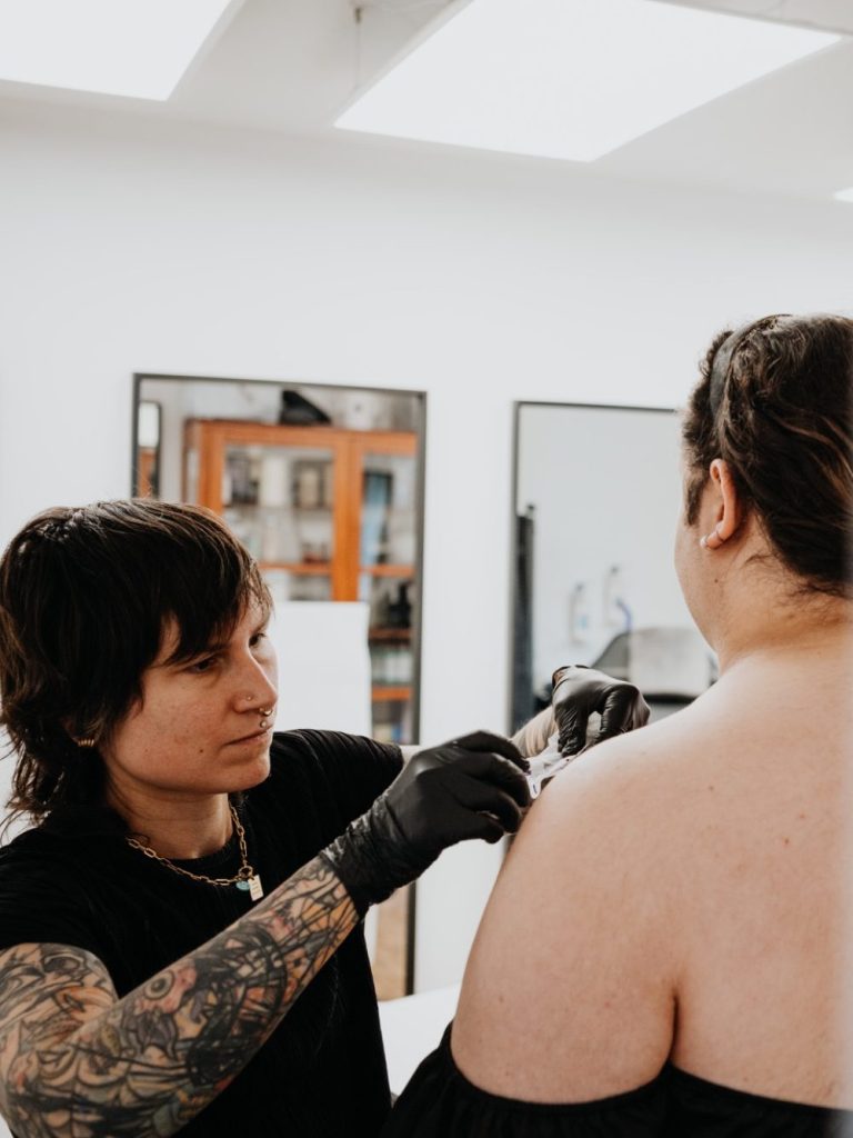 Tattoo-Künstlerin tätowiert das Schulterblatt einer Person im Studio.
