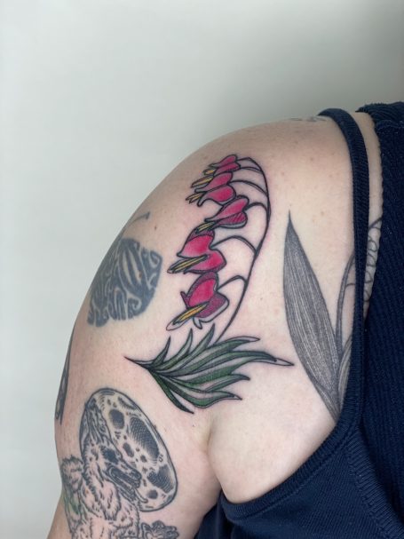 Nahaufnahme eines bunten Tattoos mit Orchideen und grünen Blättern auf einem Oberarm.