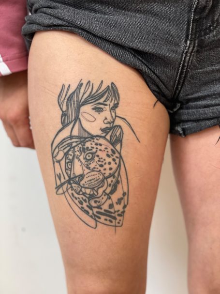 Tattoo auf dem Oberschenkel zeigt eine weibliche Figur mit einem Leoparden.