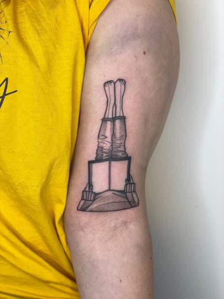 Tattoo eines Glaswerkzeugs mit zwei Ausläufen auf einem Untergrund.